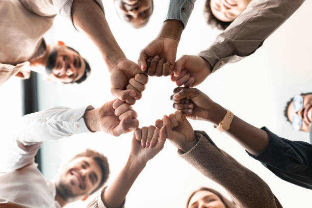 Portrait of diverse business people giving fist bump in cirle Teamwork, Power And Partnership Concept. Below view of multucultural group of smiling people making fist bump standing in circle. Workers doing fist pump together celebrating good deal corporate culture stock pictures, royalty-free photos & images