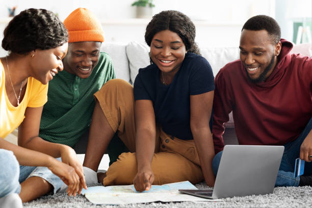 istock Smiling black friends planning vacation, using map and laptop 1322854921