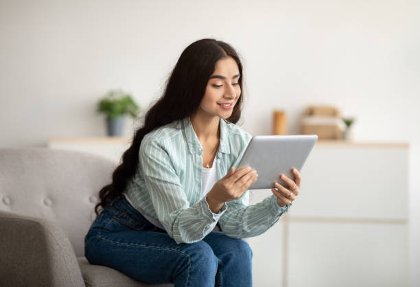 istock Cheerful Indian lady sitting in armchair with tablet computer, studying remotely or having online meeting at home 1322855986