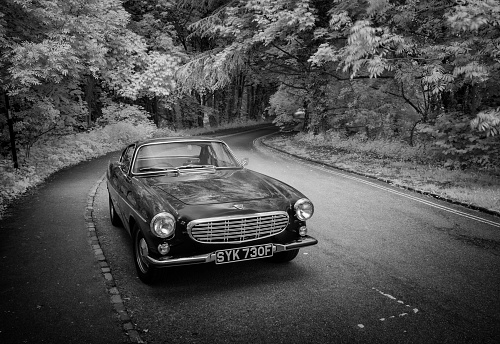 Great Missenden, UK - May 25, 2021: The sun shines down on a dark blue Volvo 1800S from 1967 parked at the side of the road. Infrared image converted in black and white.