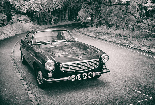 Great Missenden, UK - May 25, 2021: The sun shines down on a dark blue Volvo 1800S from 1967 parked at the side of the road. Infrared image converted in black and white.