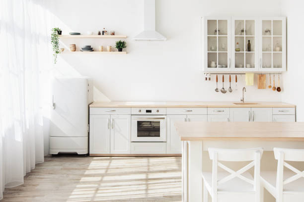 istock Light kitchen interior with white furniture and shelves, small refrigerator near window, empty space 1322858607
