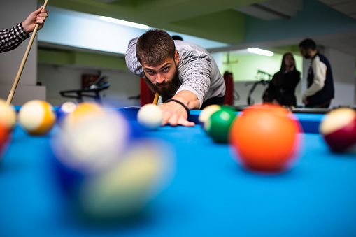 A young man is focused on his move while shooting pool
