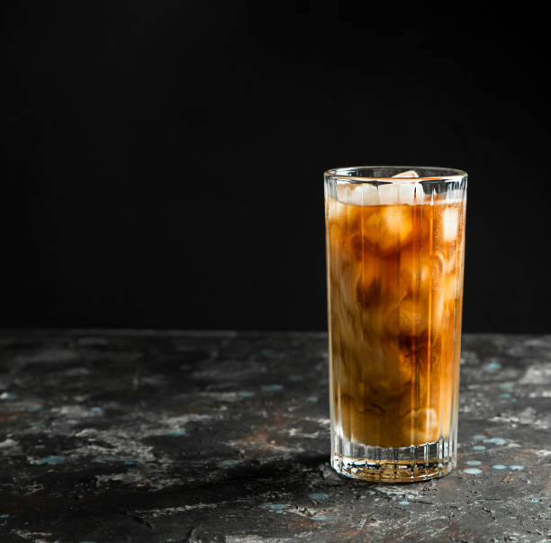 istock Cold coffee with ice and cream in a tall glass on a black background. 1322865710