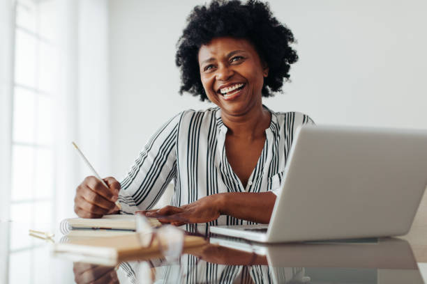 femme mature heureuse travaillant au bureau à domicile - african ethnicity women laptop computer photos et images de collection