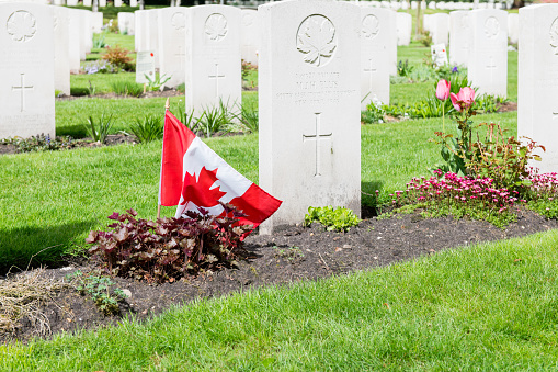 View at a number of grave stones and a small Canadia flag on the Holten Canadian War Cemetery in The Netherlands. The cemetery is the last resting place for 1355 Canadian soldiers who fell in battle while liberating The Netherlands.