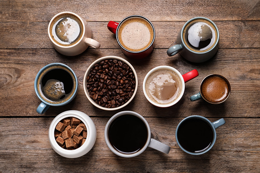 Cups of hot coffee with beans and sugar on wooden table, flat lay