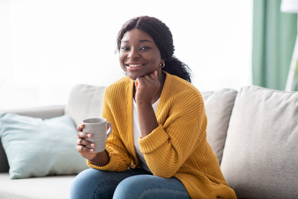 istock Beautiful african american woman sitting on sofa, drinking tea 1322870136