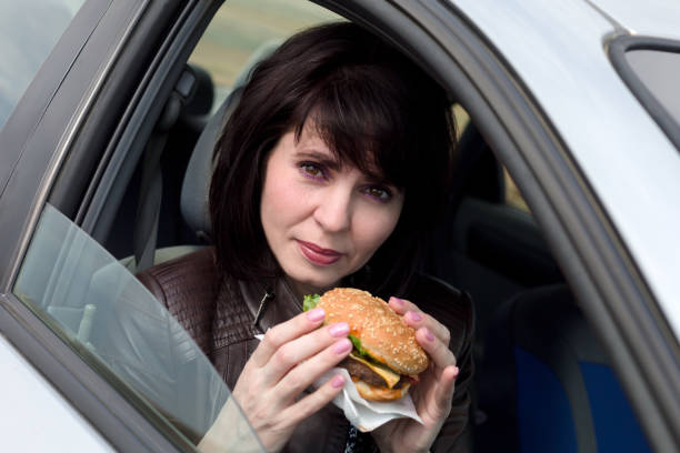 une femme dans la voiture avec un hamburger dans les mains - vehicle interior indoors window chair photos et images de collection