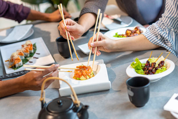 details of a table at the japanese restaurant, hands of a multiethnic group with sticks picking up fusion food, seafood, sushi and sashimi - buffet japanese cuisine lifestyles ready to eat imagens e fotografias de stock