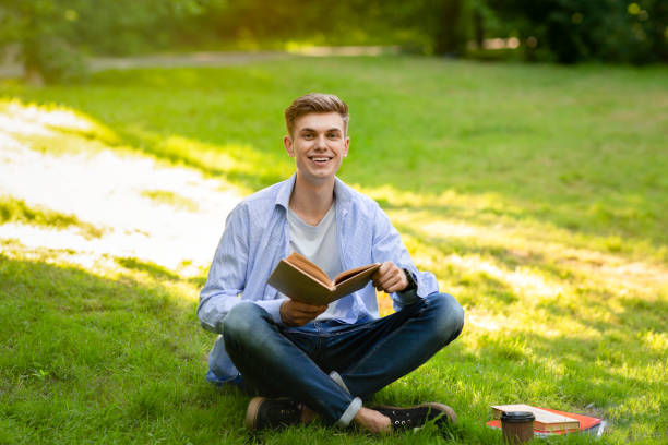 istock Teenage student guy reading book outdoors,learning at university campus yard 1322874886