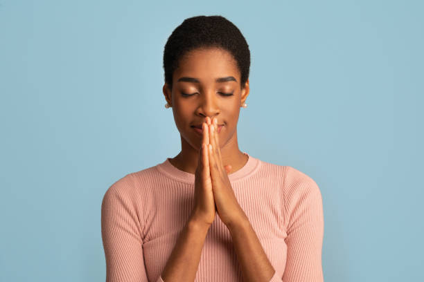 Portrait Of Beautiful Black Lady Praying With Clasped Hands Near Face Portrait Of Beautiful Black Lady Praying With Clasped Hands Near Face And Closed Eyes, Religious African American Woman Feeling Bblessed, Standing Isolated Over Blue Background, Copy Space pleading photos stock pictures, royalty-free photos & images