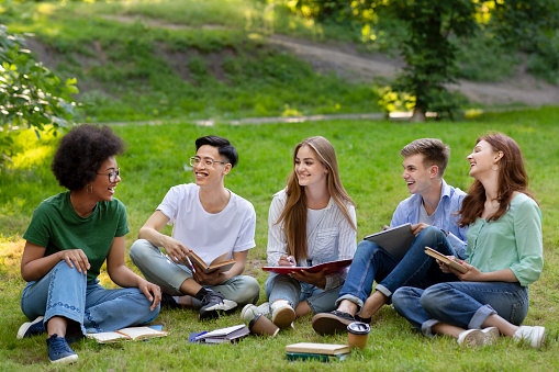 Pastime In Campus. Outdoor portrait of group of college friends resting after classes together, sitting on grass, chatting and laughing, copy space