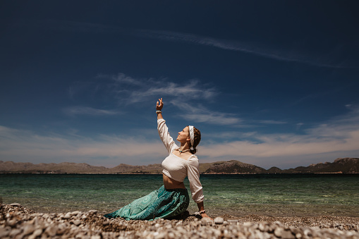 Spiritual woman in a feminin pose while doing mindfully a spiritual and sacred dance on the sunny beach in Majorca. Creative color editing. Appropriable for mindfulness concepts. Part of a series.