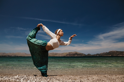 Spiritual woman in a feminin pose while doing mindfully a spiritual and sacred dance on the sunny beach in Majorca. Creative color editing. Appropriable for mindfulness concepts. Part of a series.