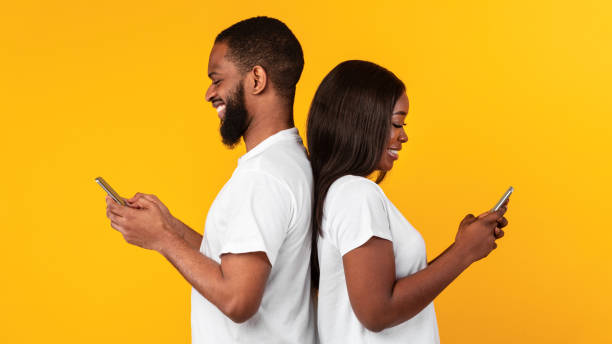 istock African american couple using smartphones, yellow studio wall 1322877650