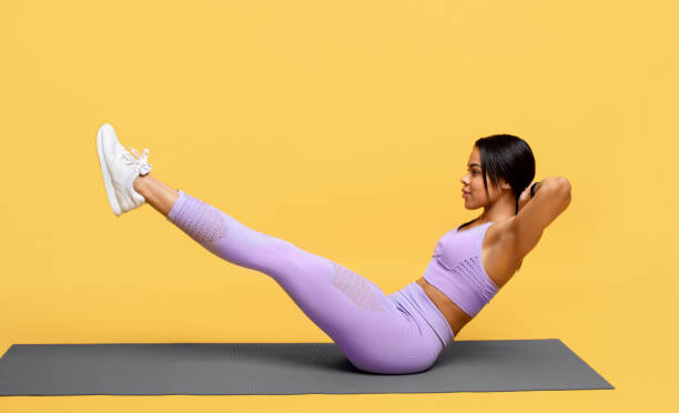 workout-konzept. sportliche afrikanische amerikanische frau tun bauchmuskeln mit erhobenen beinen auf gelbem studio-hintergrund - core strength stock-fotos und bilder