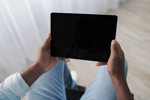 Video call, online video and mobile app during self-isolation at covid. Mature african american male disabled in wheelchair holding tablet with blank screen in living room interior, pov, copy space