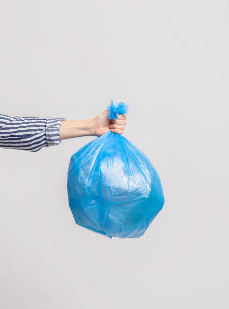 istock Female Hand Holding Blue Plastic Bag With Garbage Over Light Grey Background 1322880025