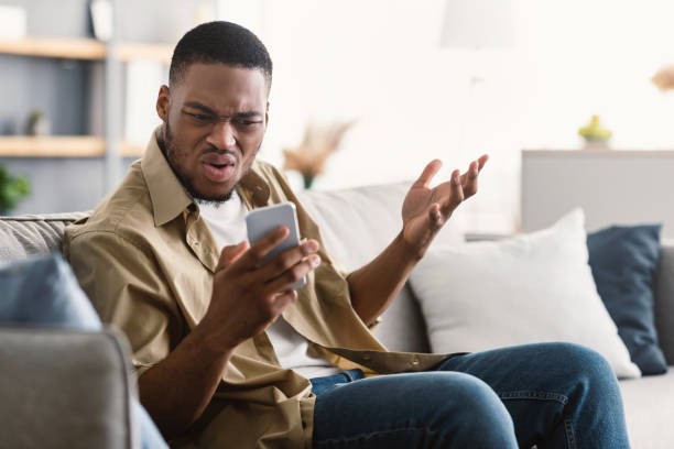 istock Discontented African American Guy Using Cellphone Having Issue At Home 1322880103