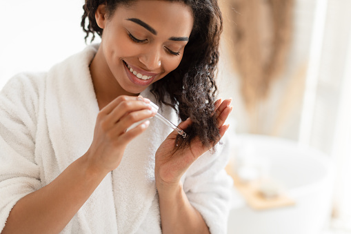 Mujer afroamericana aplicando suero en el cabello dañado en el baño photo