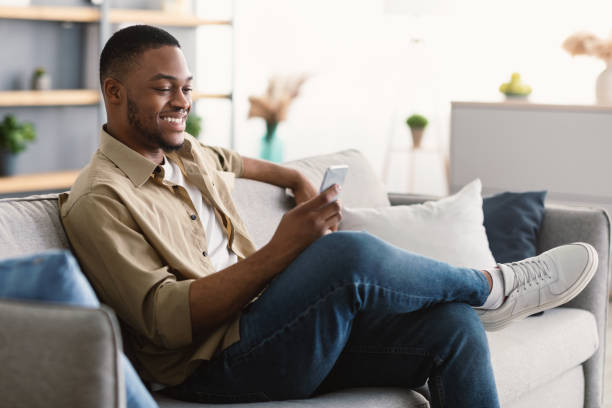 istock Happy African American Man Using Phone Texting Sitting At Home 1322880756