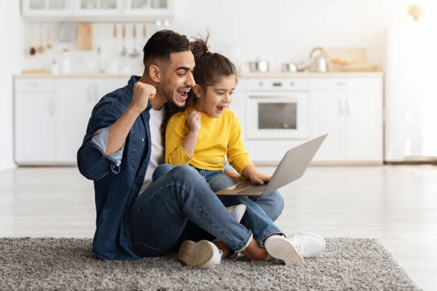 jovem pai árabe e filhinha celebrando sucesso com laptop em casa - sale relationships loving indoors - fotografias e filmes do acervo