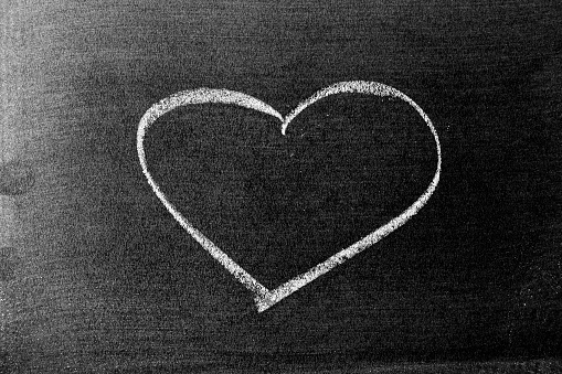 White color chalk hand drawing in heart shape on blackboard or chalkboard background
