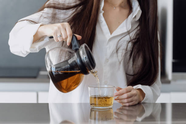 Young woman pouring herbal tea from teapot in cup