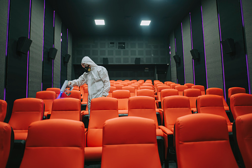 asian chinese cinema cleaner worker with Respirator Mask protective workwear performing disinfection in cinema hall on chairs and carpet before the movie show time