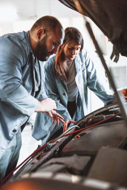 istock Mechanic Teacher Asking Female Student About Car Engine Parts During Practical Exam 1322882641