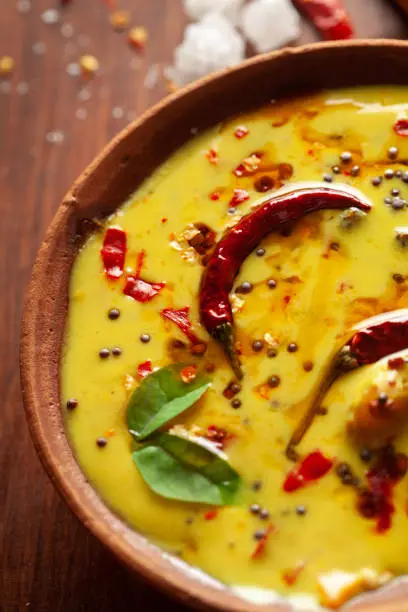 Photo of Close-up of Indian kadi or kadhi pakora with it basic ingredients. Garnished with green curry-patta leaves and red chili flacks. Over wooden top background.