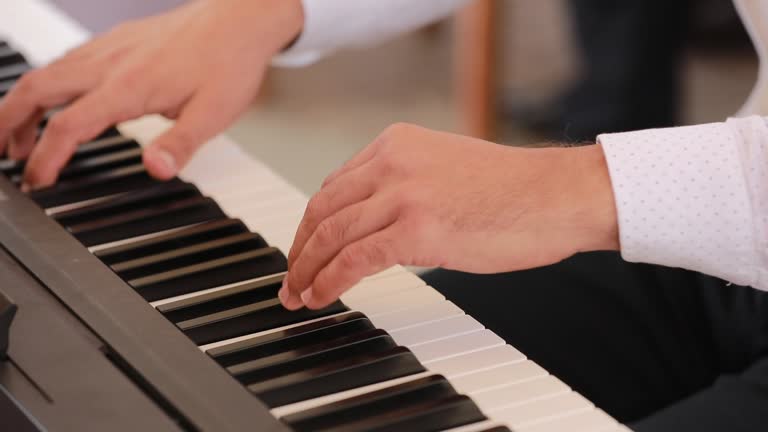 Close up of hands as young man sits at grand piano and plays at home.