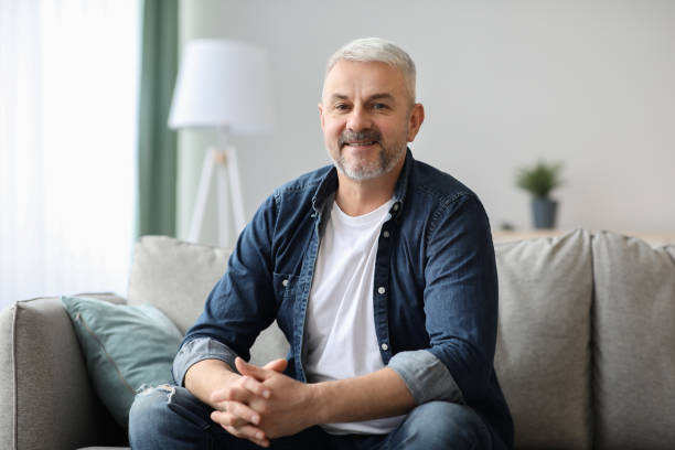 istock Handsome grey-haired elderly man posing on couch in living room 1322885658