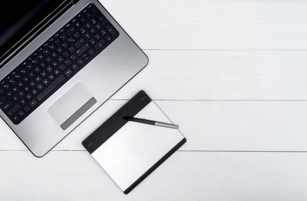 istock Wooden white office desk table with open blank laptop computer and graphic tablet, free space. Top view with copy space. Grey laptop with graphic tablet on wooden table background 1322886024