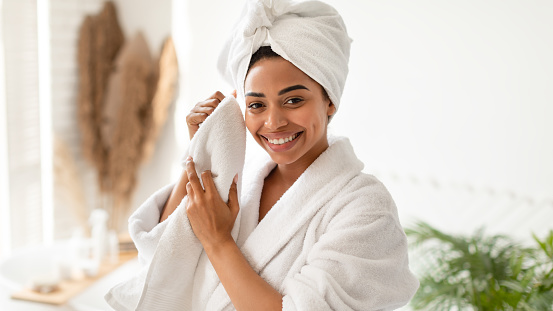 Happy African American Female Drying Face With Soft Towel After Bathing Caring For Skin In Modern Bathroom At Home, Smiling Looking At Camera. Skincare And Beauty Routine Concept. Panorama