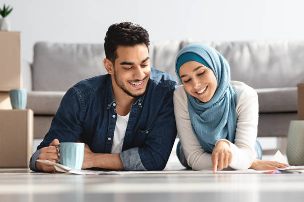 istock Happy middle-eastern couple laying on floor with apartment plan 1322887292