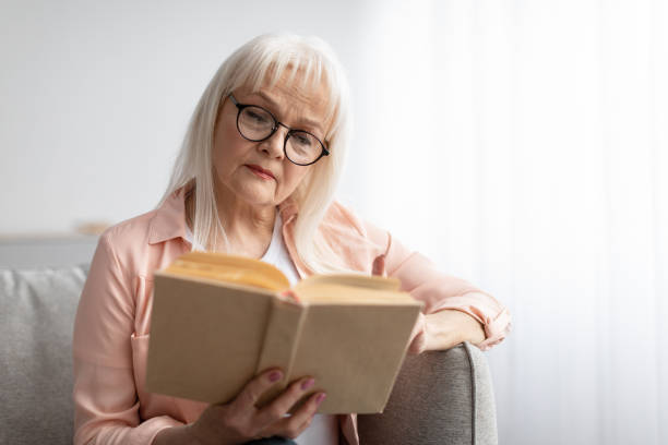 istock Focused mature woman in glasses reading book 1322888281
