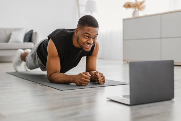 istock Black Guy Doing Elbow Plank Exercise At Laptop Training Indoors 1322889628