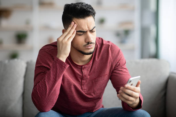 istock Closeup of thoughtful arab guy sitting on couch, using smartphone 1322889666