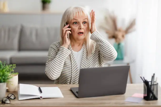 Photo of Surprised shocked mature woman talking on mobile phone