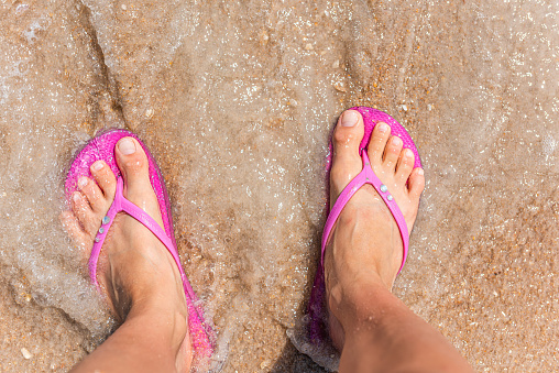Flat top above view down of brown orange sea sand in Marineland, Florida beach with woman feet pink slippers flip-flops with wave crashing on shore