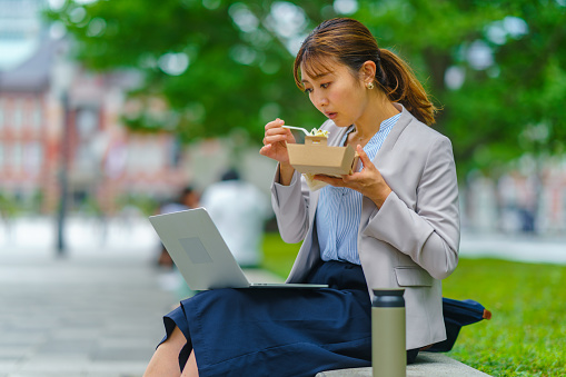 A businesswoman is working on a laptop while having lunch in the city.