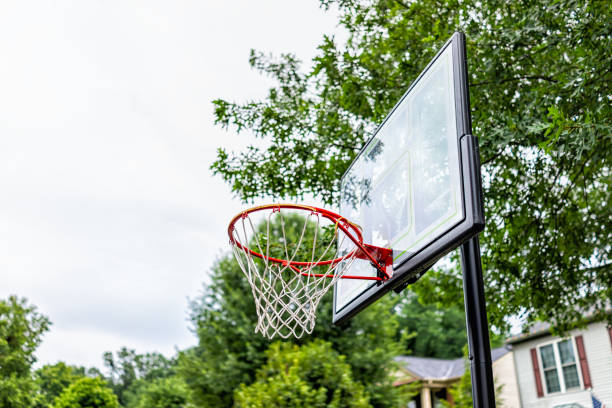 primo piano del canestro da basket rosso con rete e tavola di vetro nel parco giochi guardando il cielo e la casa sullo sfondo - basketball slam dunk basketball hoop sport foto e immagini stock