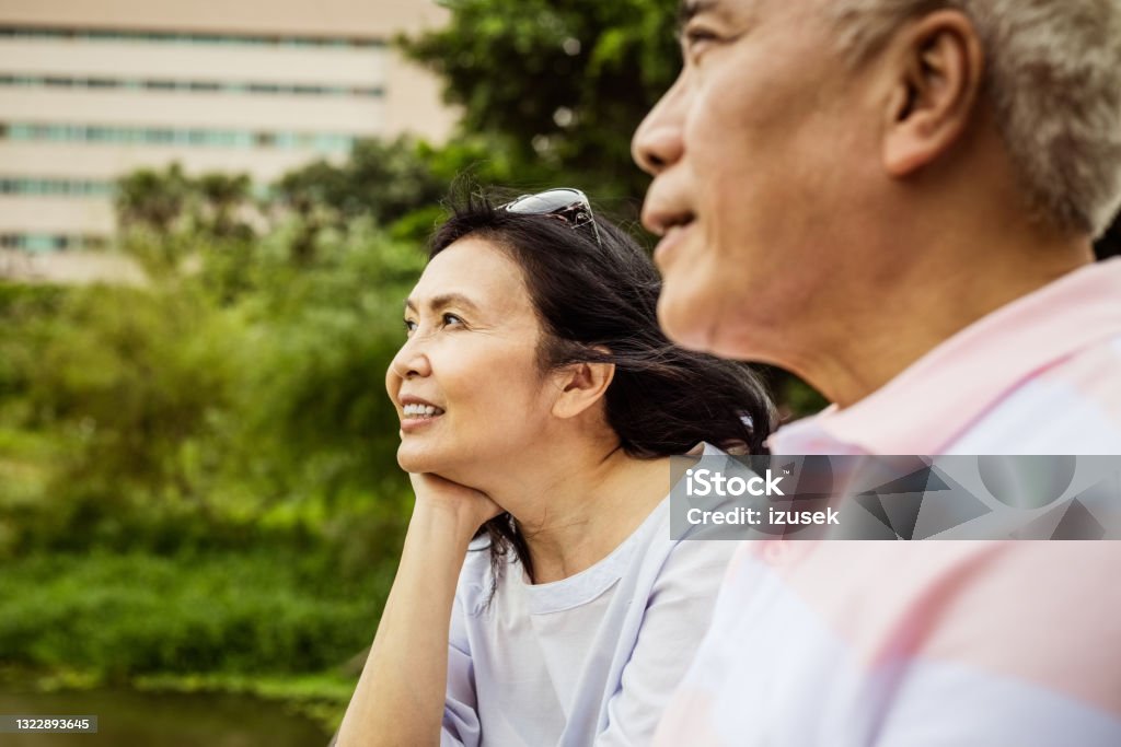 Senior couple relaxing in the park Senior woman and man sitting in the park in the city, close up of faces. Asian couple enjoying time together. Introspection Stock Photo