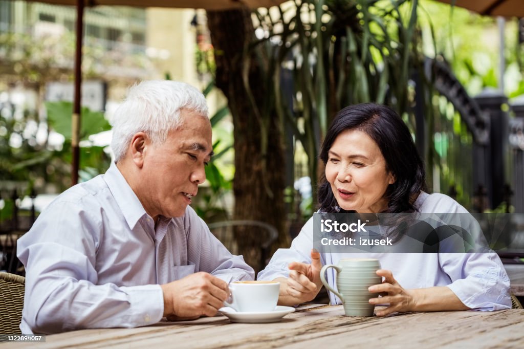 Senior couple talking in outdoor cafe Senior woman and man sitting at the table in small cafe, talking and drinking coffee. Asian couple enjoying time together. Couple - Relationship Stock Photo
