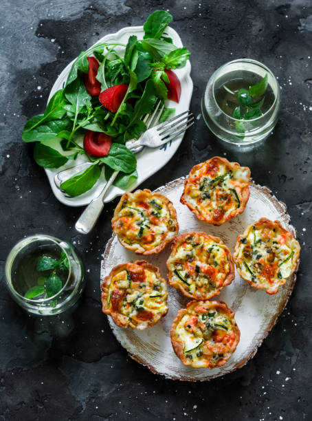 istock Aperitif table - mini quiche with salmon and zucchini, fresh tomato arugula salad and mint cocktail on a dark background, top view 1322894800