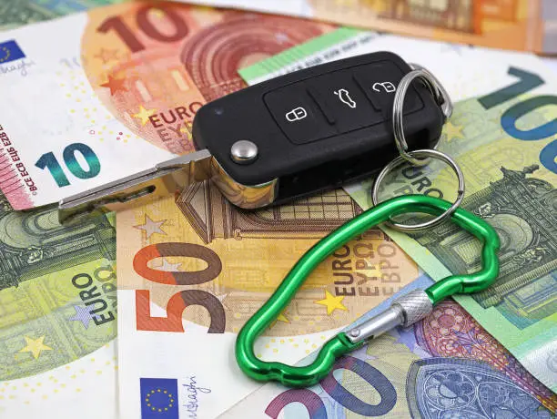 Photo of car key with carabiner in car shape on euro money background, concept of car insurance