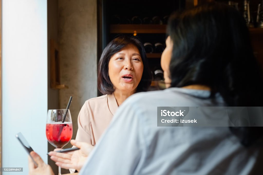 Senior friends enjoying drink in cafe Senior women sitting at the table in small cafe over drinks, watching smart phone. Asian friends enjoying time together. 60-69 Years Stock Photo