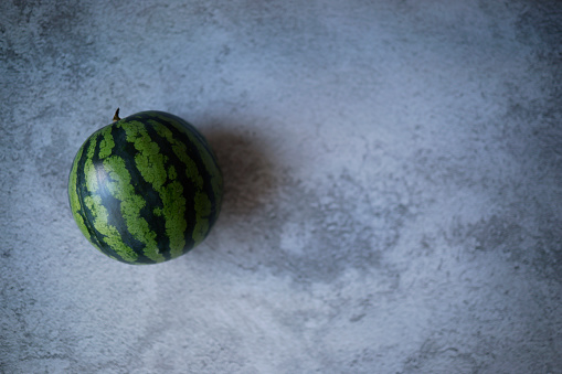 Istanbul, Turkey-June 10, 2021: A small round watermelon with light-dark green stripes on a gray rough concrete floor. Shot with Canon EOS R5.
